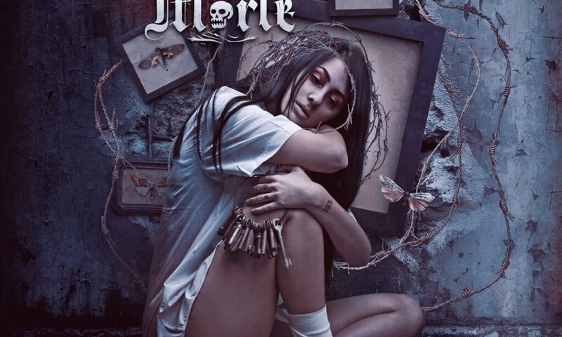 The album cover for Crime of Passion by Belle Morte presents a pale, solemn woman sitting curled on a cushion, surrounded by barbed wire and framed moths. She wears a torn white shirt and bandages, with bullets draped at her waist and a crown of thorns on her head. The band’s ornate logo and the album title in cursive.