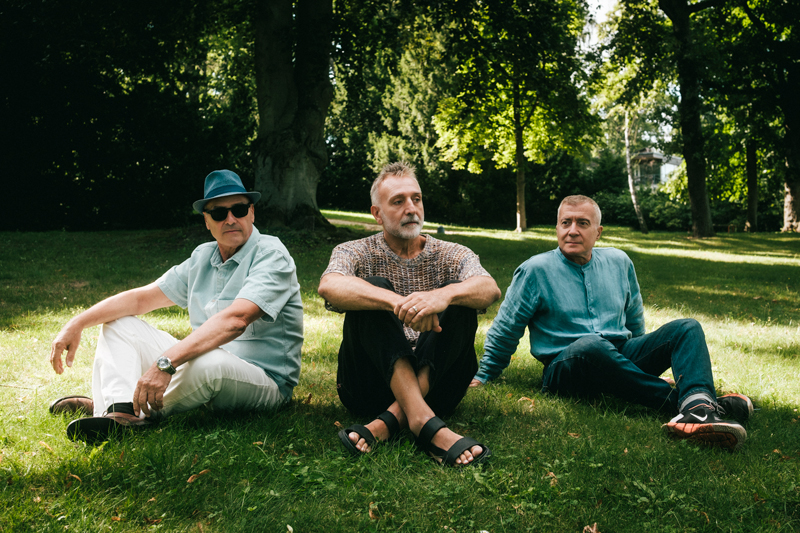 Cervello - Photo by Michele Piazza. the three surviving members sitting on the grass.