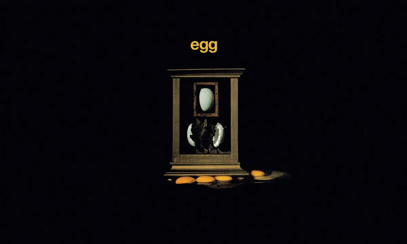 Egg - Egg cover artwork. A black background with a wooden frame in the middle that features a whole egg on top and a cracked egg below and then some egg yolks underneath.