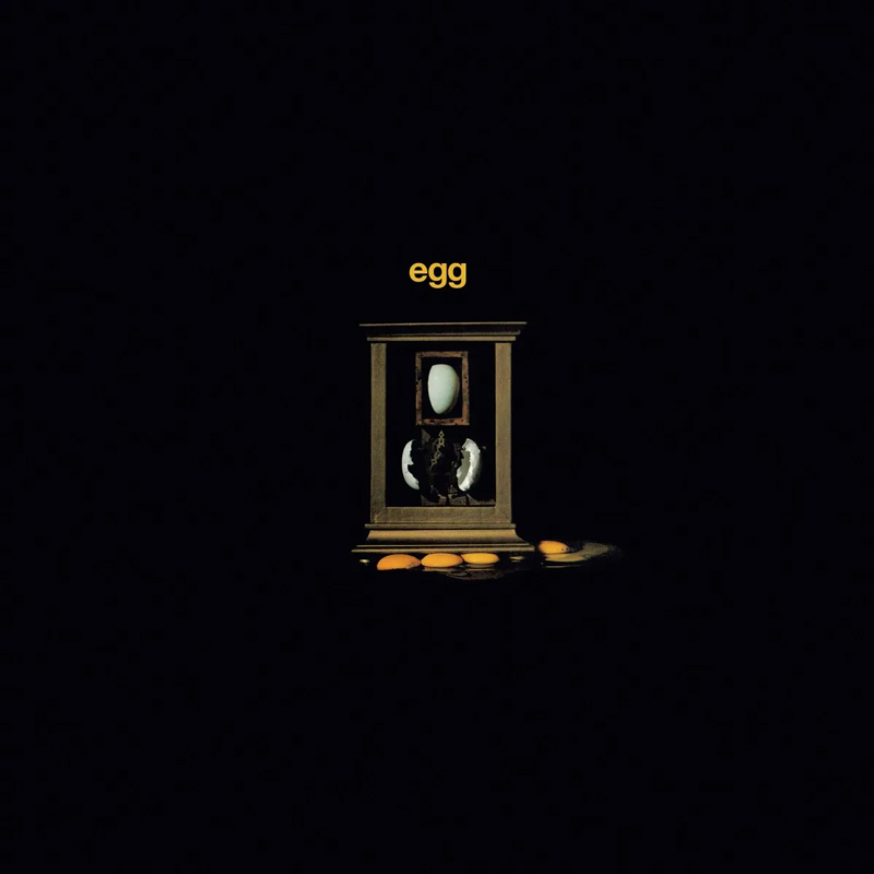 Egg - Egg cover artwork. A black background with a wooden frame in the middle that features a whole egg on top and a cracked egg below and then some egg yolks underneath.