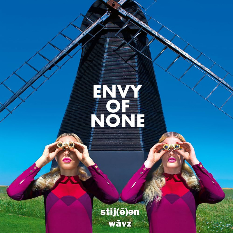 The album cover for Envy of None – Stygian Wavz features a hyper-saturated image of two identical blonde women in futuristic magenta outfits, peering through binoculars. They stand in front of a towering black windmill under a blue sky. The title appears boldly in white block letters, while the album name is stylized below in phonetic typography.
