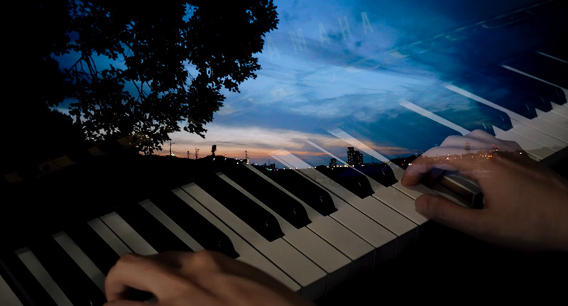 A combination of two images: a nighttime cityscape and two hands playing a keyboard.