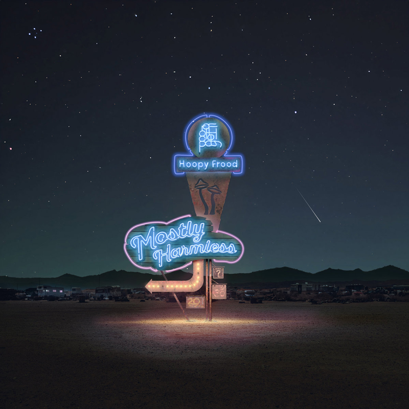 The album cover shows a neon roadside sign glowing in the desert night. It reads "Hoopy Frood" at the top and "Mostly Harmless" in a retro cursive font below, with a lit arrow pointing left. There is a starry sky and faint shooting star in the background.