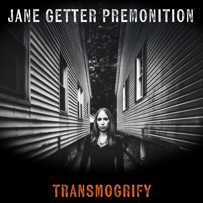 Jane Getter Premonition - Transmogrify cover artwork. A black-and-white image of a solitary woman in a narrow alley between two converging houses.