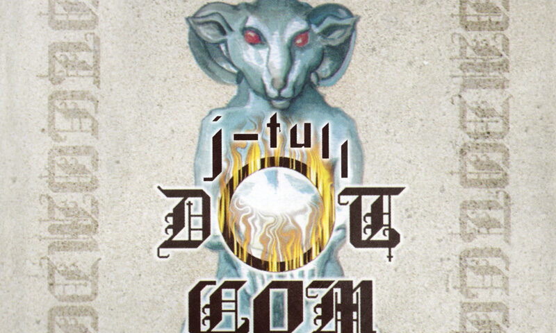 Jethro Tull J-Tull Dot Com Another Cast Of The Net cover artwork. The cover features a pale blue, ram-like humanoid figure with glowing red eyes, seated and holding a luminous white orb surrounded by golden flames.