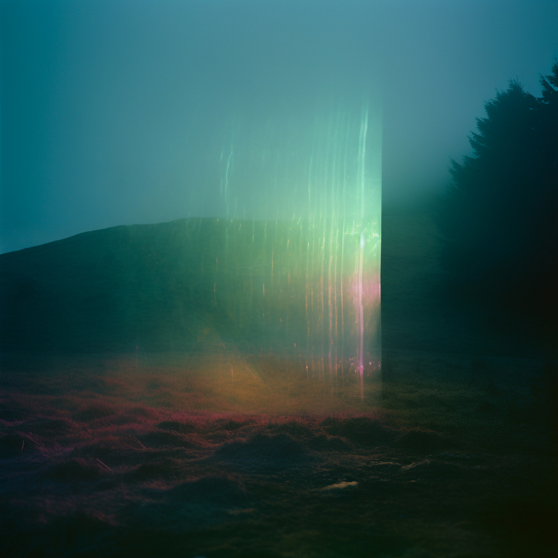 Johan Agebjorn - Southern-Forest cover artwork. A misty landscape fills the frame, tinted in deep teal and magenta hues. In the center, a tall glowing rectangular prism emits rainbow light, casting faint reflections onto the grassy ground. A dark hill rises in the background while a silhouette of trees stands at the right edge, partially swallowed by fog.