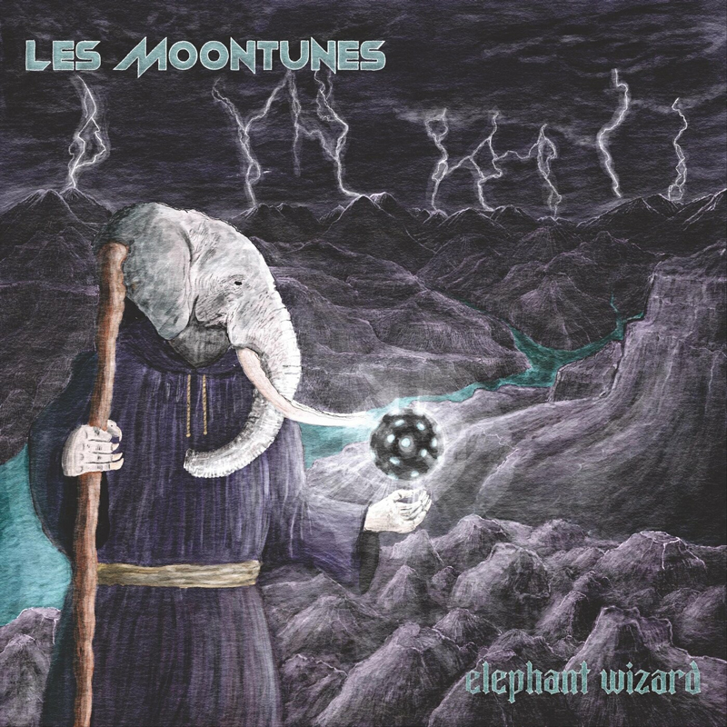 The album cover for Elephant Wizard by Les Moontunes depicts a robed, elephant-headed wizard standing in a jagged mountain landscape beneath a storm-dark sky. Lightning splits the clouds overhead as the figure grips a staff in one hand and holds a glowing, geometric orb in the other. Purples, grays, and blues dominate the scene.