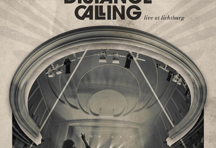 The cover presents a sepia-toned photograph of a grand concert hall viewed from the back of the audience. A sweeping, arched ceiling frames the stage below, where beams of light illuminate the band in the distance. In the foreground, a silhouetted figure raises an arm toward the stage. At the top, uppercase lettering reads “Long Distance Calling,” with “live at lichtburg” in smaller type beneath it.