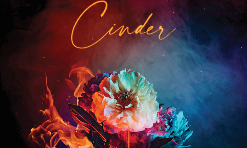 The cover of Cinder by Lux Terminus features a bouquet of vividly colored flowers engulfed in flames, set against a smoky, gradient background that shifts from deep red to blue. The album title is written in elegant, glowing script, while the band name appears above in sleek, modern sans-serif type.