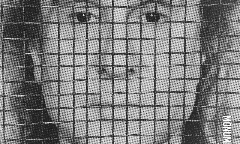 The album cover for Monumentata by Nad Sylvan features a grayscale, close-up photo of Sylvan’s face, obscured by a grid or mesh overlay. The artist's name appears in small white text in the top left, while the album title is rotated vertically in the bottom right.