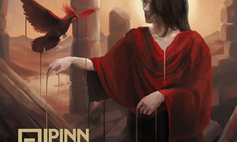 The album cover for For The Love of Drama by Pinn Dropp depicts a scene set among ancient ruins. A person draped in a flowing red robe extends an arm toward a red bird that appears to be tethered or bleeding, with streaks of red connecting them. The background glows with warm light from a low sun, framed by broken stone arches and barren desert terrain. The band’s logo and title appear in gold lettering at the lower left.