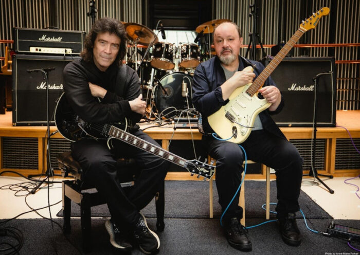Steve Hackett and Steve Rothery sitting in a studio holding electric guitars.