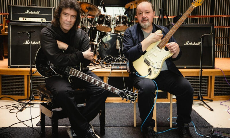 Steve Hackett and Steve Rothery sitting in a studio holding electric guitars.