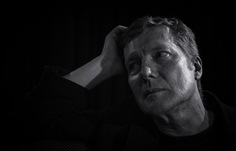 Tim Bowness - photo by Leon Barker. Black and white of the artist leaning on his right hand.