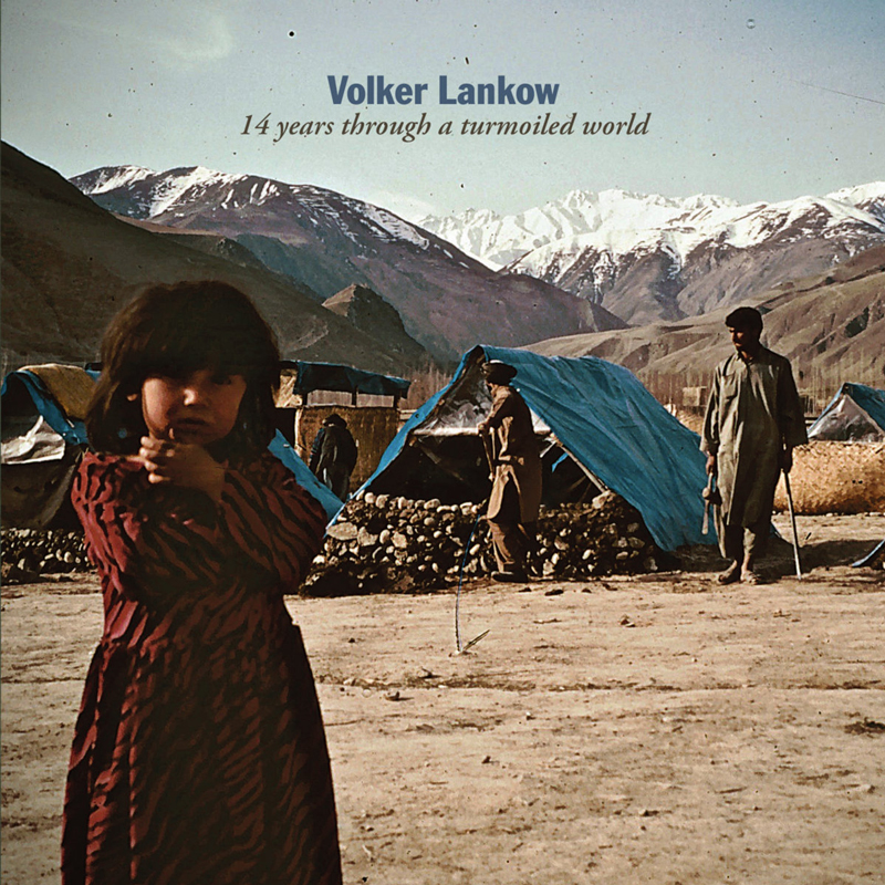 The album cover for Volker Lankow’s 14 Years Through A Turmoiled World features a young girl in the foreground, while men and makeshift shelters with blue tarps occupy the background, set against snow-capped mountains.